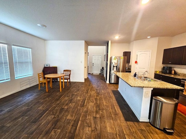 kitchen with sink, dark brown cabinetry, an island with sink, dark hardwood / wood-style flooring, and stainless steel fridge with ice dispenser