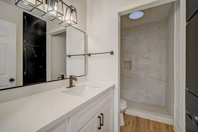 bathroom featuring a tile shower, vanity, wood-type flooring, and toilet