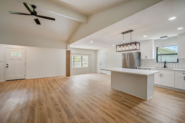 kitchen with stainless steel fridge, a center island, lofted ceiling with beams, white cabinets, and decorative light fixtures