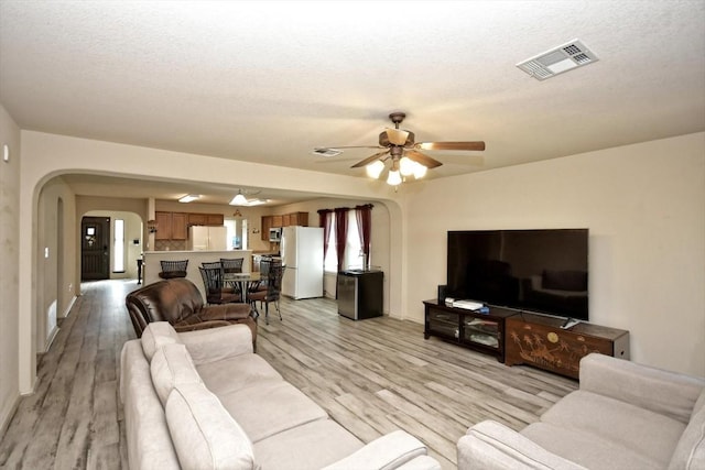 living room with a textured ceiling, ceiling fan, and light wood-type flooring