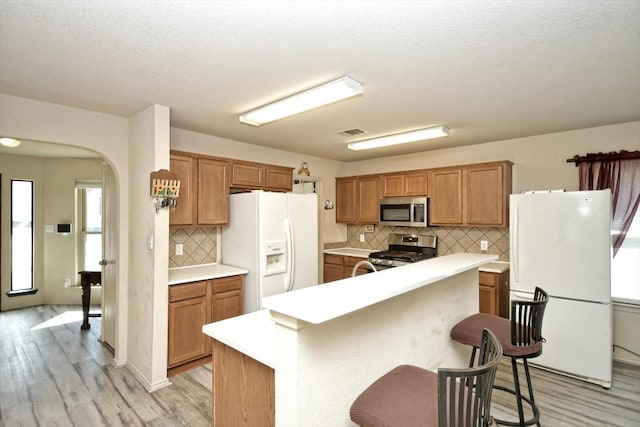 kitchen with tasteful backsplash, a center island, light wood-type flooring, appliances with stainless steel finishes, and a kitchen breakfast bar