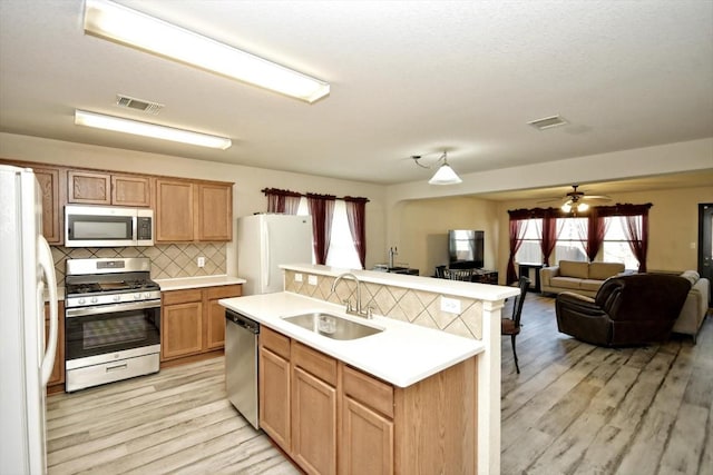 kitchen with sink, light wood-type flooring, an island with sink, stainless steel appliances, and backsplash