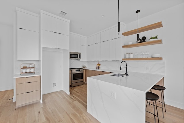 kitchen featuring sink, white cabinets, a kitchen breakfast bar, hanging light fixtures, and stainless steel appliances