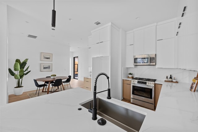 kitchen featuring stainless steel appliances, light stone countertops, sink, and white cabinets