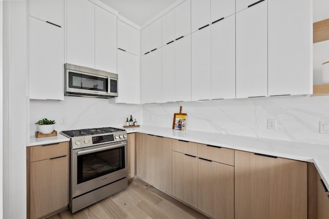 kitchen featuring tasteful backsplash, white cabinetry, appliances with stainless steel finishes, and light wood-type flooring