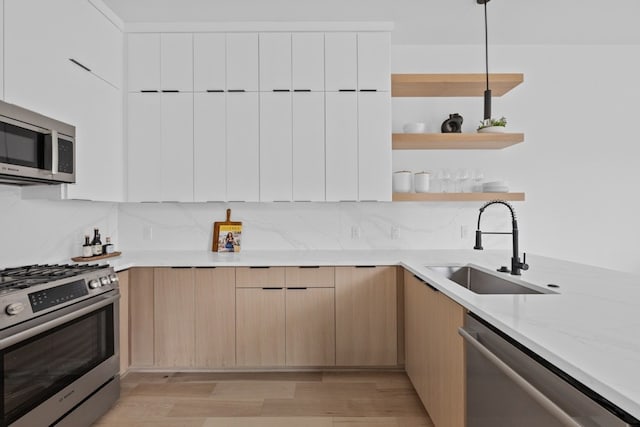 kitchen featuring pendant lighting, sink, white cabinets, light stone counters, and stainless steel appliances