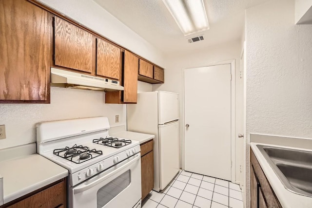 kitchen featuring sink, white appliances, a textured ceiling, and light tile patterned flooring