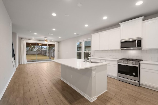 kitchen with sink, stainless steel appliances, white cabinets, and a center island with sink