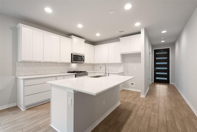 kitchen featuring sink, white cabinetry, stainless steel appliances, tasteful backsplash, and a center island with sink