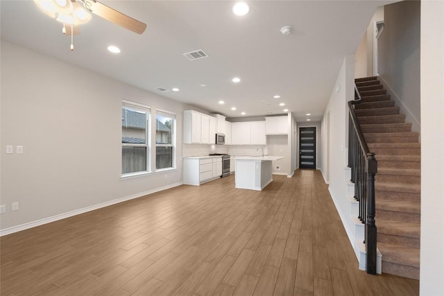 kitchen featuring white cabinetry, light hardwood / wood-style flooring, a kitchen island, stainless steel appliances, and decorative backsplash