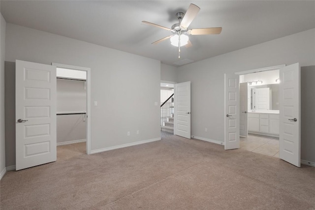 unfurnished bedroom featuring connected bathroom, a walk in closet, light colored carpet, and ceiling fan