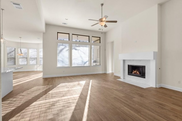 unfurnished living room with hardwood / wood-style flooring, ceiling fan, a towering ceiling, and a high end fireplace