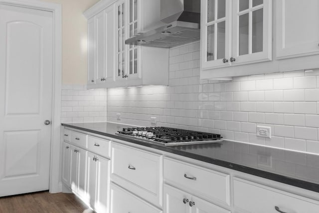 kitchen with dark wood-type flooring, white cabinets, backsplash, and wall chimney range hood