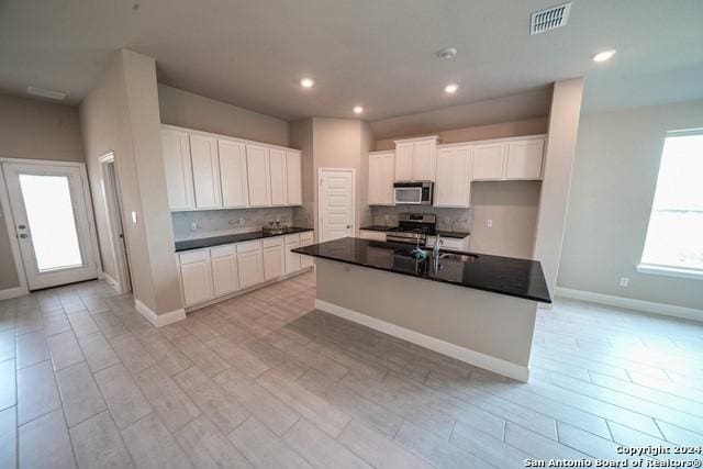 kitchen featuring white cabinetry, a center island with sink, tasteful backsplash, and appliances with stainless steel finishes