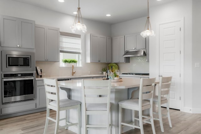 kitchen with a kitchen island, gray cabinetry, backsplash, stainless steel appliances, and light hardwood / wood-style flooring