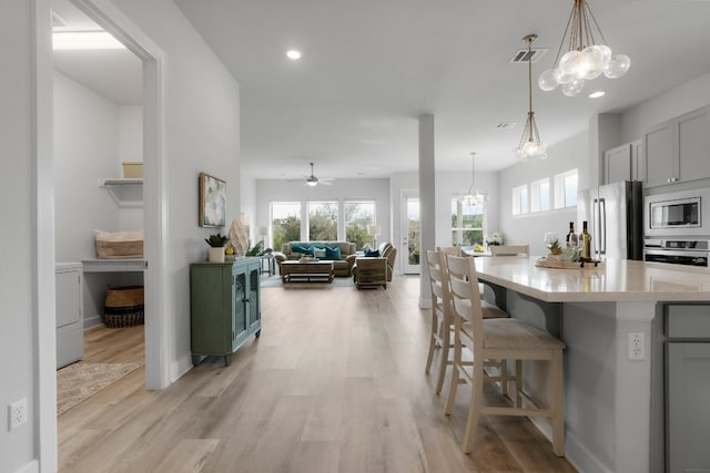 kitchen featuring stainless steel appliances, hanging light fixtures, a kitchen bar, and light hardwood / wood-style flooring