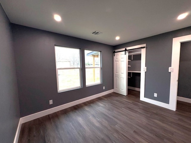 unfurnished bedroom featuring a barn door, dark hardwood / wood-style flooring, and a spacious closet