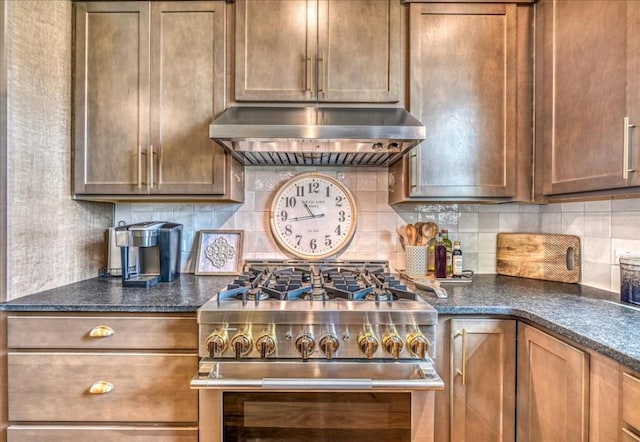 kitchen with tasteful backsplash, stainless steel stove, range hood, and dark stone counters