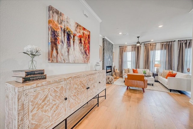 interior space with crown molding, a large fireplace, ceiling fan, and light hardwood / wood-style floors