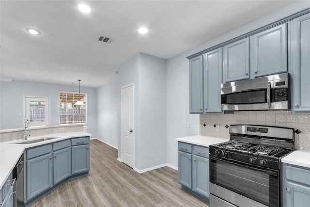 kitchen with decorative light fixtures, tasteful backsplash, sink, stainless steel appliances, and light wood-type flooring