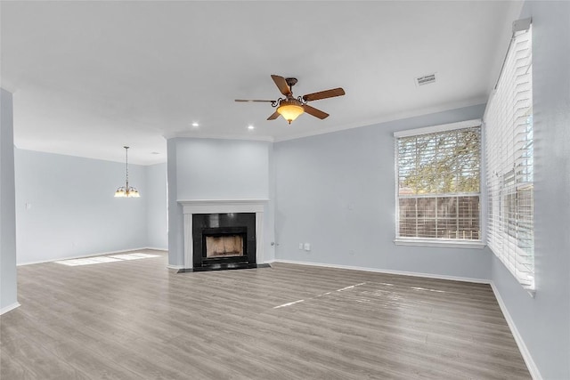 unfurnished living room with wood-type flooring, ceiling fan with notable chandelier, and crown molding