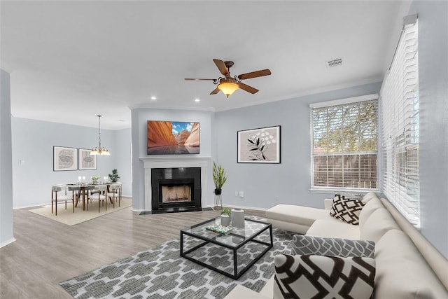 living room with hardwood / wood-style flooring, ornamental molding, and ceiling fan with notable chandelier