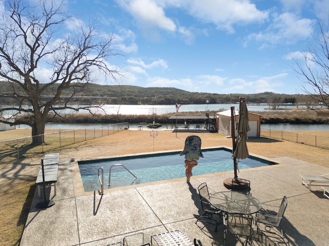 view of swimming pool with a water view, a storage shed, and a patio