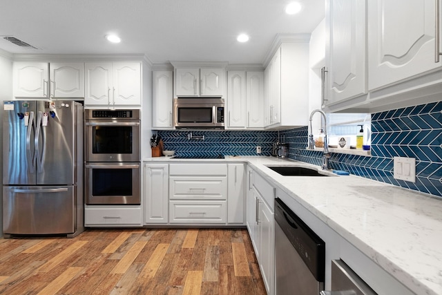 kitchen with stainless steel appliances, white cabinetry, light stone countertops, and sink