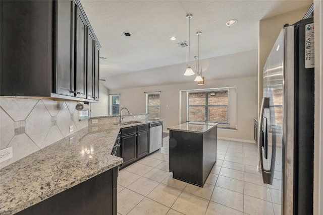 kitchen featuring appliances with stainless steel finishes, sink, hanging light fixtures, a center island, and light stone counters