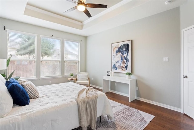 bedroom featuring dark wood-type flooring, ornamental molding, a raised ceiling, and ceiling fan