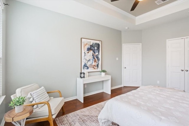 bedroom with ornamental molding, ceiling fan, a tray ceiling, dark wood-type flooring, and a closet