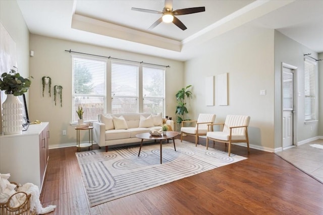 living room with dark hardwood / wood-style floors, ceiling fan, and a tray ceiling