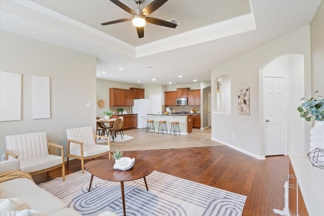 living room with crown molding, a tray ceiling, light hardwood / wood-style flooring, and ceiling fan