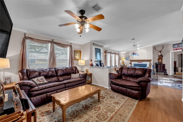 living room with ceiling fan, lofted ceiling, a tile fireplace, and light wood-type flooring