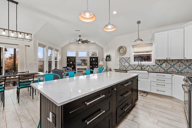 kitchen with hanging light fixtures, vaulted ceiling, white cabinets, and a kitchen island