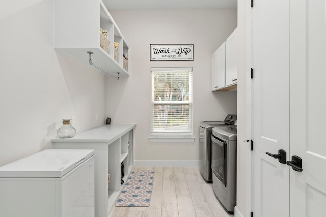 clothes washing area with cabinets, washing machine and dryer, and light hardwood / wood-style flooring