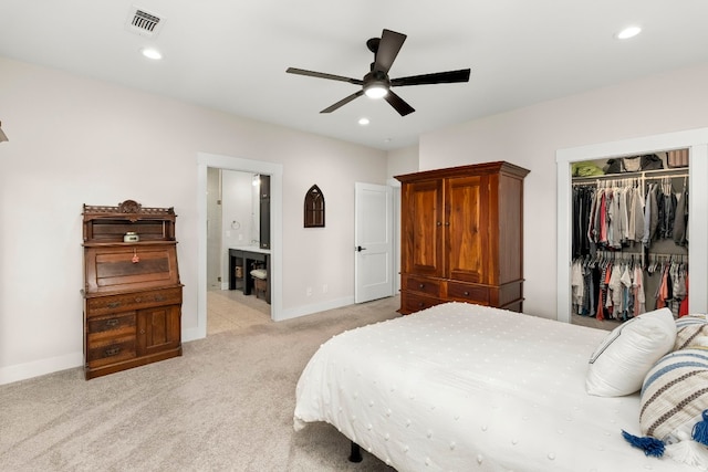 bedroom with ensuite bathroom, light colored carpet, ceiling fan, and a closet