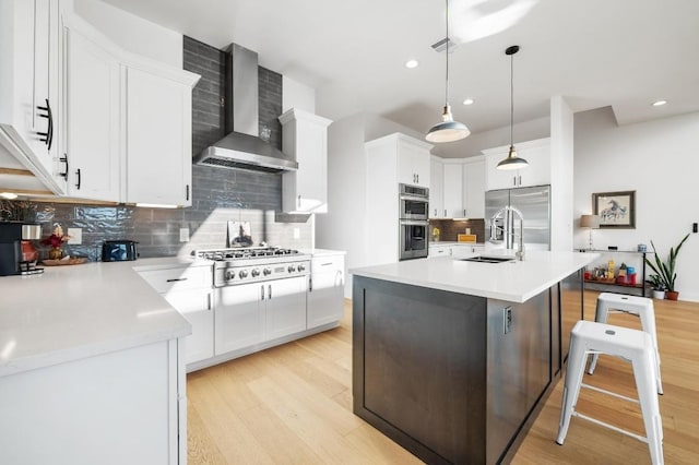 kitchen with pendant lighting, white cabinets, a kitchen island with sink, stainless steel appliances, and wall chimney range hood