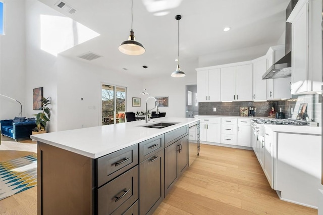 kitchen with pendant lighting, sink, light hardwood / wood-style flooring, a kitchen island with sink, and white cabinets