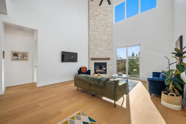 living room with hardwood / wood-style floors, a stone fireplace, and a towering ceiling