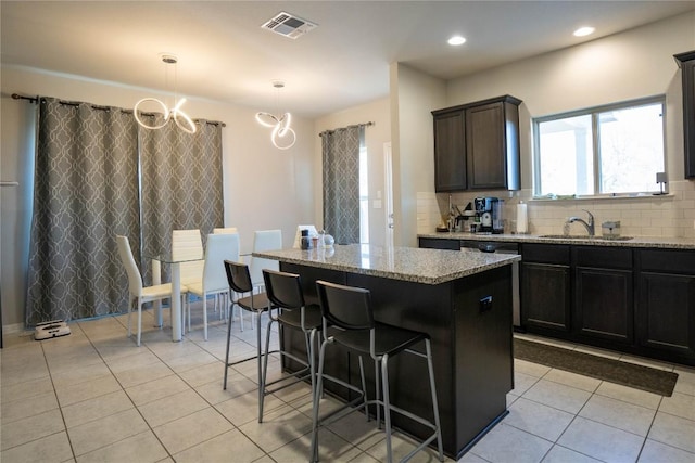 kitchen with a breakfast bar area, hanging light fixtures, a kitchen island, light stone countertops, and decorative backsplash