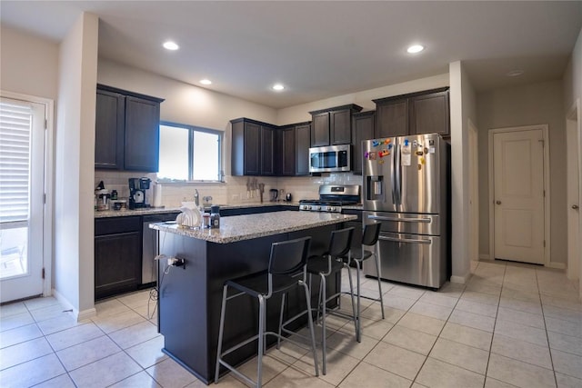 kitchen with stainless steel appliances, a center island, light stone counters, a kitchen bar, and decorative backsplash