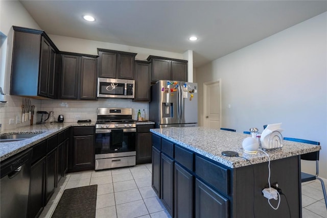 kitchen featuring light tile patterned floors, appliances with stainless steel finishes, a center island, light stone counters, and decorative backsplash