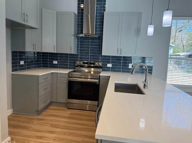 kitchen featuring wall chimney range hood, sink, stainless steel range with electric stovetop, decorative backsplash, and light wood-type flooring