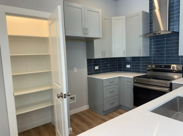 kitchen with stainless steel electric range oven, tasteful backsplash, gray cabinetry, hardwood / wood-style flooring, and wall chimney range hood