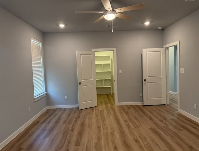 unfurnished bedroom with hardwood / wood-style floors, a walk in closet, a closet, and ceiling fan