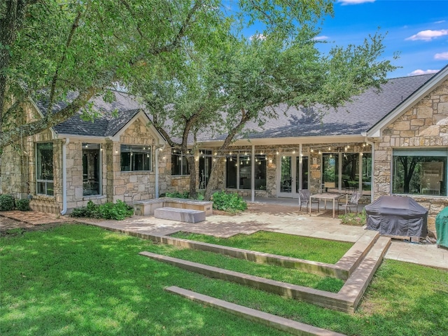 rear view of house featuring a patio area, a lawn, and stone siding