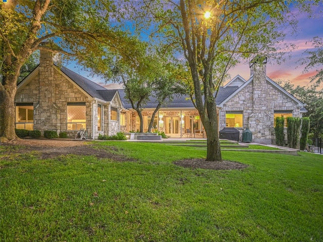 exterior space with a chimney, a yard, and stone siding
