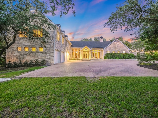 view of front of house featuring stone siding, an attached garage, a front lawn, and driveway