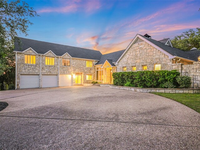 shingle-style home with a garage, driveway, and stone siding